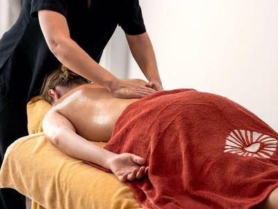 Person erhält Massage auf einem Massagetisch, Körper mit orangefarbenem Handtuch bedeckt.