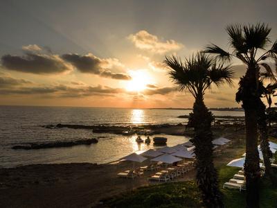 Sonnenuntergang über einem Strand mit Palmen und Liegestühlen in einem Hotelresort.