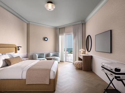 Modernes Hotelzimmer mit Doppelbett, Sesseln und Balkon mit Meerblick.