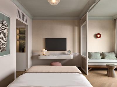 Modern eingerichtetes Hotelzimmer mit Bett, Wandmonitor und gemütlichem Sitzbereich.