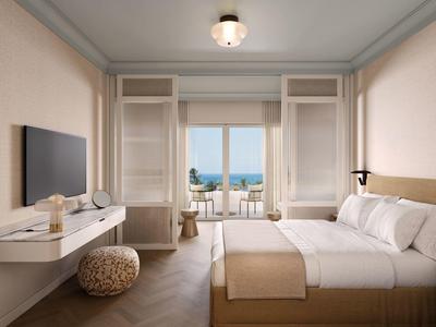 Helles Hotelzimmer mit Doppelbett, Meerblick und Balkon mit Sitzgelegenheiten.