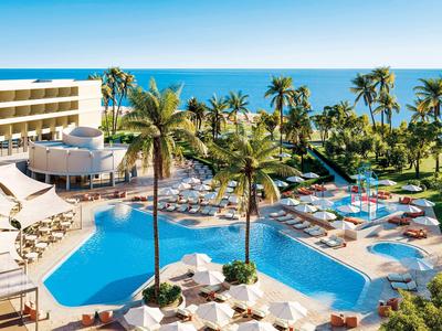 Piscina dell'hotel con lettini, palme e vista sul mare in una giornata soleggiata