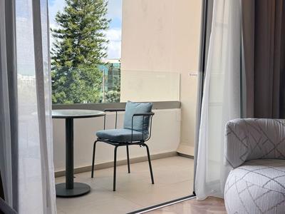 Balcone con piccolo tavolo rotondo e una sedia blu, tende parzialmente aperte.