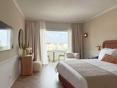 Camera d'hotel moderna con letto grande, zona soggiorno e balcone con vista sulla città.