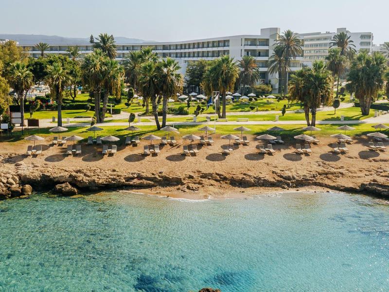Langgestrecktes Hotel am Strand mit Palmen und klarem blauem Wasser im Vordergrund.