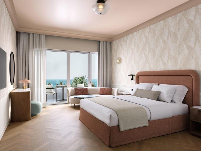 Modernes Hotelzimmer mit Doppelbett, Meerblick und Balkon mit Sitzgelegenheiten.