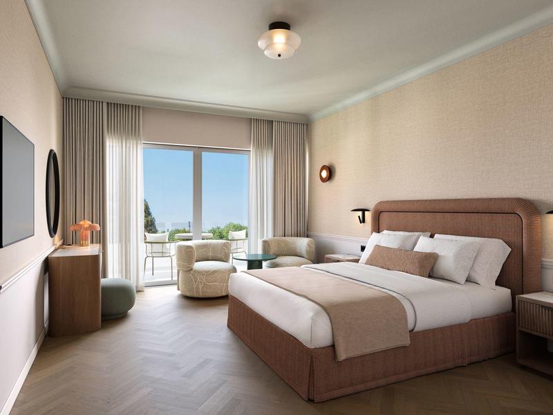 Helles Hotelzimmer mit großem Doppelbett, Sitzbereich und Balkon mit Meerblick.