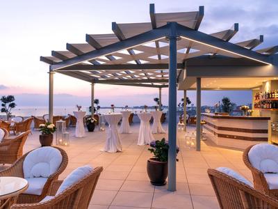Elegante Hotelterrasse mit Sitzbereichen und Bar, Blick auf das Meer bei Dämmerung.