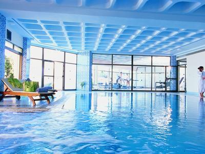 Piscina interna con grandi finestre, lettini e due persone in accappatoio