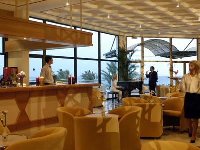 Lounge dell'hotel con bar, poltrone e grandi finestre con vista sulle palme.