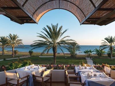 Terrazza di un hotel con tavoli apparecchiati e vista su palme e mare.