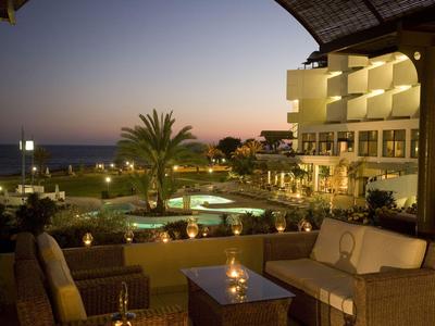 Taras hotelowy o zmierzchu z miejscami do siedzenia, basenem i widokiem na morze.