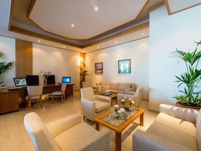 Lounge d'hotel moderna con aree salotto, piante e computer su pavimento in legno.