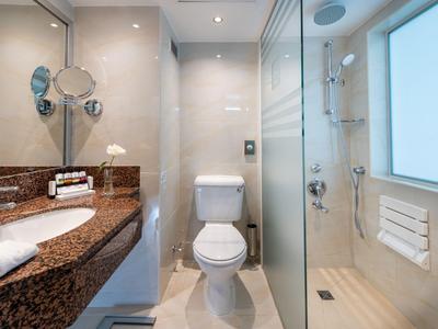 Nowoczesna łazienka hotelowa z toaletą, umywalką i szklaną kabiną prysznicową w świetle dziennym.