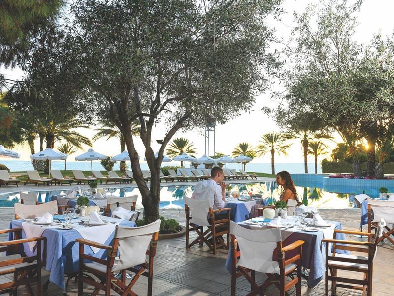 Außenbereich eines Restaurants mit gedeckten Tischen, Bäumen und Blick auf den Pool.