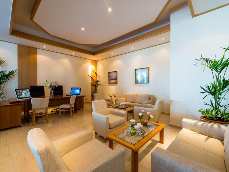 Moderner Warteraum mit Beistelltisch, Sessel, Sofa, Pflanzen und zwei Arbeitsplätzen mit Computern.