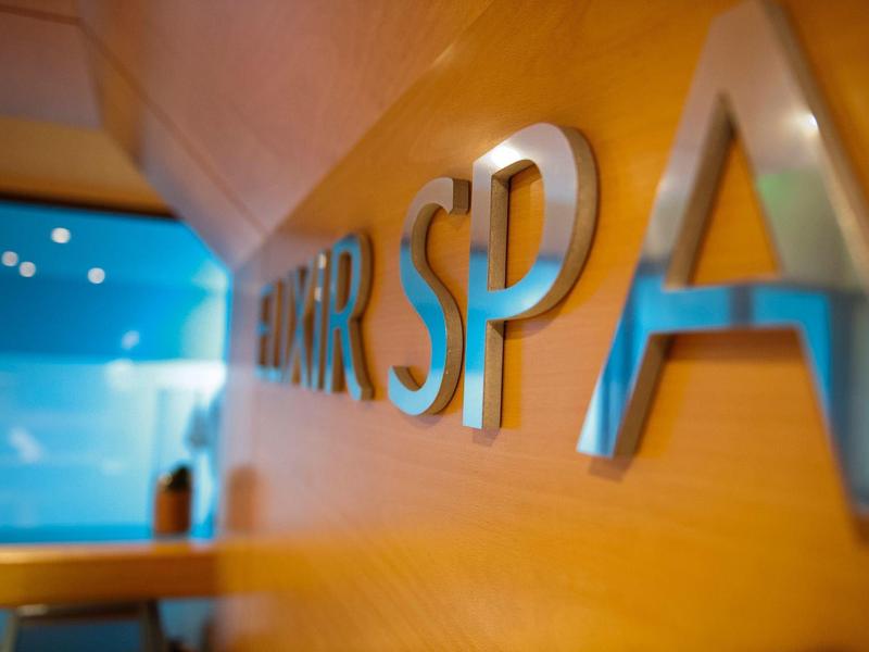 Metallene Buchstaben "SPA" an orangefarbener Wand mit verschwommenem blauen Hintergrund.