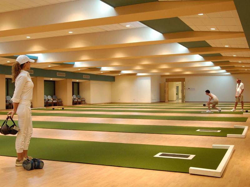 Großer Yoga-Raum mit grünen Matten, Holzfußboden und mehreren Personen beim Vorbereiten.