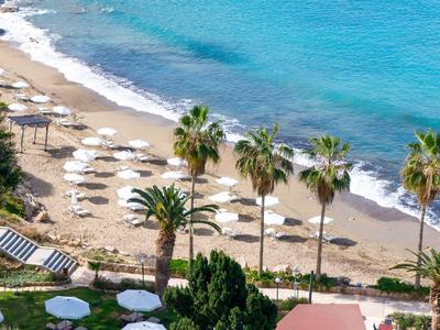 Strand mit Palmen, Sonnenschirmen und blauem Meer an einem Hotel in Küstennähe.