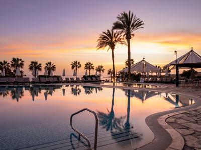 Ruhepool und Palmen bei Sonnenuntergang in einem tropischen Hotelresort.