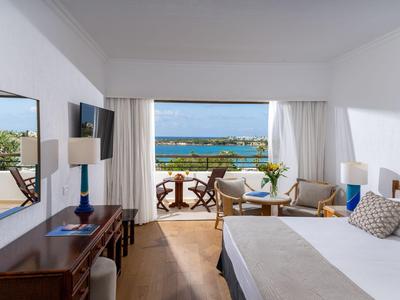 Helles Hotelzimmer mit Doppelbett, Balkon und Meerblick bei klarem Wetter.