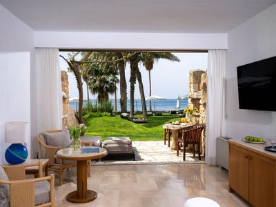 Blick von einem Hotelzimmer auf einen Garten mit Palmen und Meer im Hintergrund.