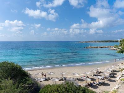 Strand mit Sonnenschirmen und Liegestühlen am klaren blauen Meer unter blauem Himmel mit Wolken.