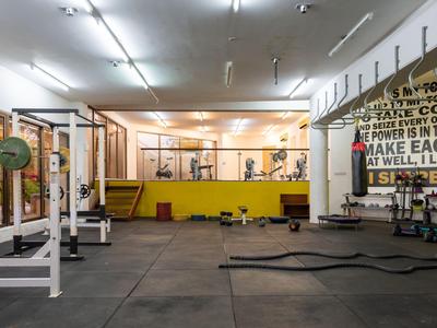 Großer Fitnessraum mit gelben Wänden, mehreren Gewichten und Seilen auf schwarzem Boden.