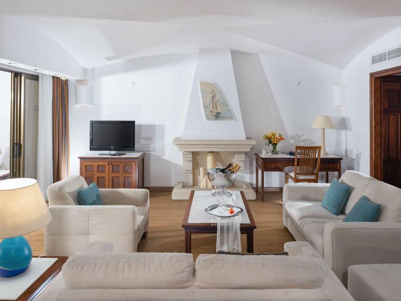 Helles Wohnzimmer mit weißen Wänden, Kamin, drei Sofas und Holzfußboden, dekoriert mit Lampen und Kissen.