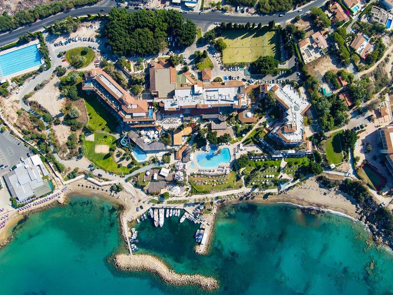 Luftaufnahme einer Küstenanlage mit Gebäuden, Straßen, Swimmingpools und Bootsanleger.