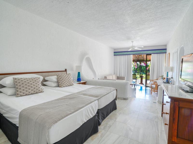 Helles, modernes Hotelzimmer mit Doppelbett, Schlafsofa, Fernseher und Terrasse mit Blick ins Grüne.