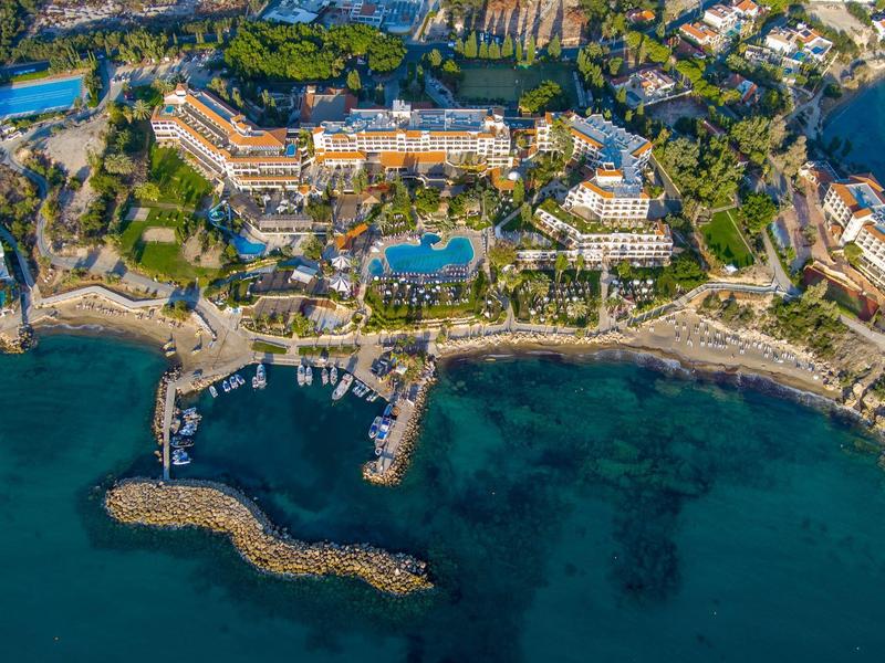 Luftaufnahme einer Küstenanlage mit Strand, Hafen, klar blauem Wasser und vielen Gebäuden.