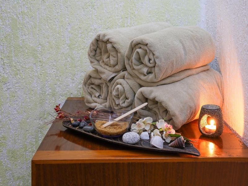 Vier zusammengerollte Handtücher liegen auf einem Holztisch neben dekorativen Steinen und einer kleinen Kerze.