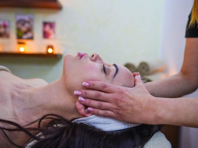 Eine Frau liegt entspannt, während eine andere ihr sanft das Gesicht massiert.