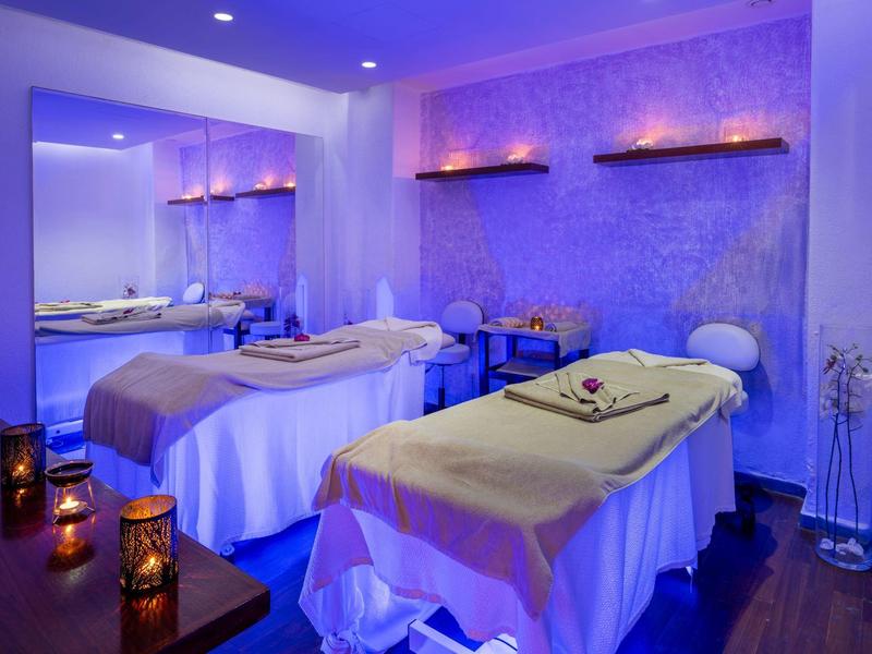 Einruhiger Massageraum mit zwei Liegen, gedämpftem blauem Licht und brennenden Kerzen.