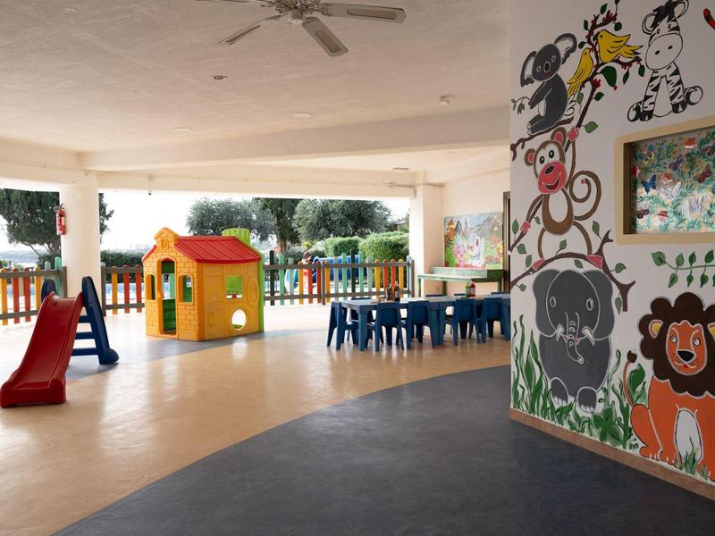 Kinderzimmer mit buntem Klettergerüst, Spielhaus, blauen Stühlen und Wandmalerei mit Tieren.