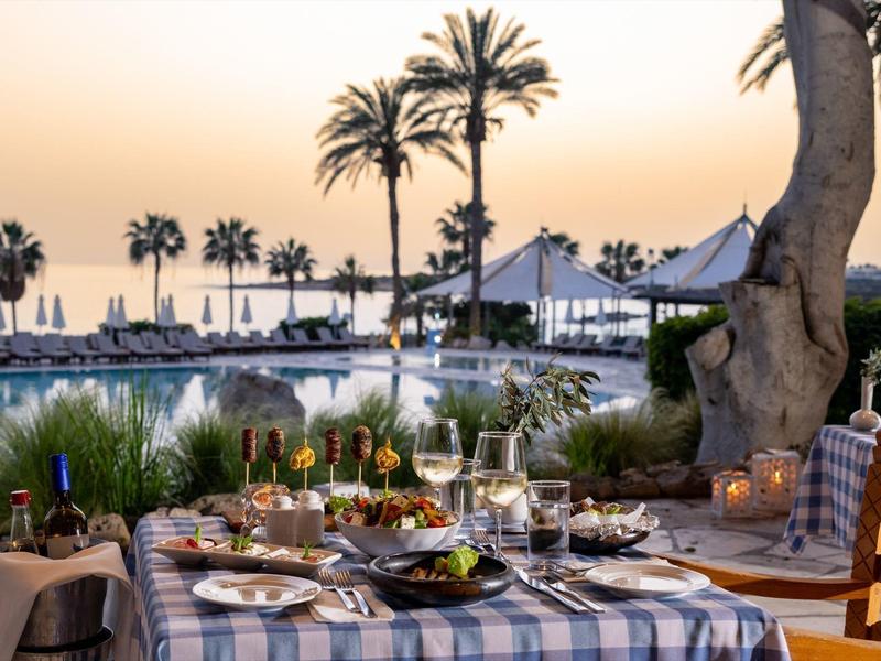 Restaurantterrasse am Meer mit gedecktem Tisch, Palmen und Sonnenuntergang im Hintergrund.