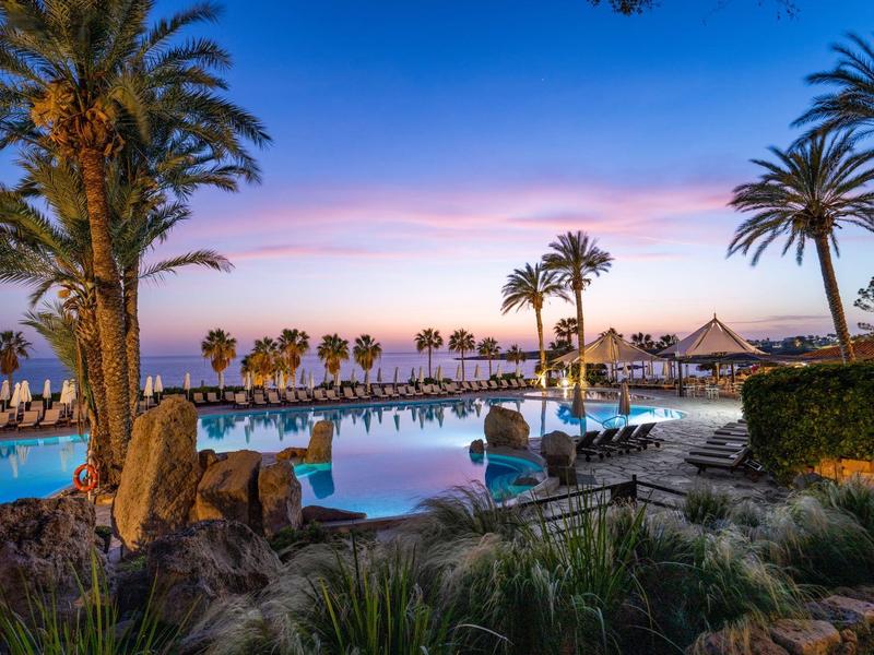 Schwimmbad mit Palmen und Liegestühlen bei Sonnenuntergang im tropischen Hotelgarten.