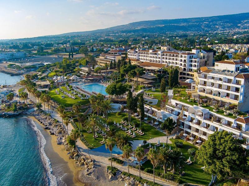 Strand mit Sand und Palmen, daneben große Hotels und Hügel im Hintergrund bei klarem Himmel.