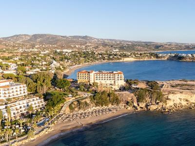 Luftaufnahme eines Küstenhotels mit Sandstrand und klarem blauem Meer umgeben von Hügeln.