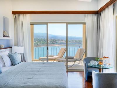 Hotelzimmer mit Meerblick, zwei Liegestühlen auf Balkon, hellen Vorhängen und modernem Ambiente.