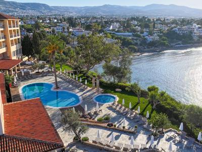 Hotel mit Außenpools, grünen Gartenanlagen und Blick auf das Meer an einem sonnigen Tag.