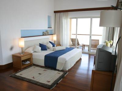 Helles Schlafzimmer mit Holzboden, Doppelbett, Nachttisch, Teppich und Balkon mit Aussicht.