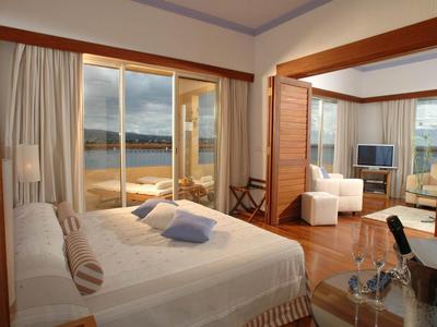 Modernes Schlafzimmer mit Doppelbett und angrenzendem Wohnzimmer mit weißen Sesseln und TV.