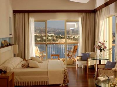 Helles Schlafzimmer mit Doppelbett, Balkon und Blick auf Wasser und Hügel. Holzboden, helle Vorhänge.