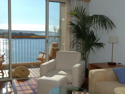 Wohnzimmer mit hellen Möbeln, Pflanzen und großer Glasschiebetür mit Meerblick und Balkon.