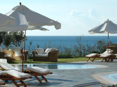 Poolbereich mit Liegestühlen und Sonnenschirmen mit Blick aufs Meer