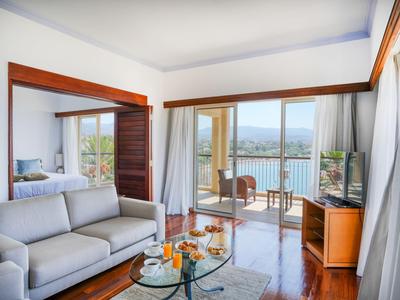 Modernes Hotelzimmer mit Sofa, Glastisch und Balkon mit Blick auf das Meer.