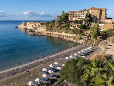 Hotel am felsigen Küstenabschnitt mit kleinem Strand und klar blauem Wasser.