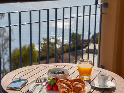 Frühstück mit Croissants, Saft und Kaffee auf einem Tisch mit Meerblick und Balkon.